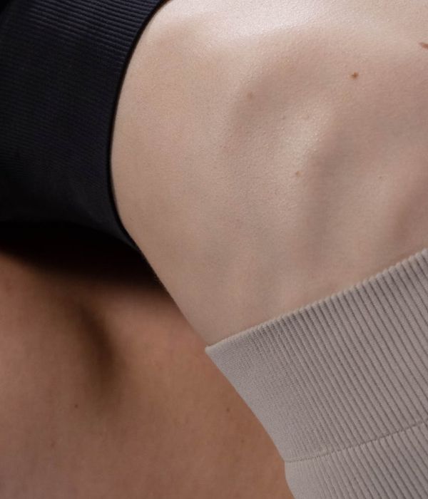 A man in athletic wear performing a controlled bodyweight exercise in a dark, minimalist setting.